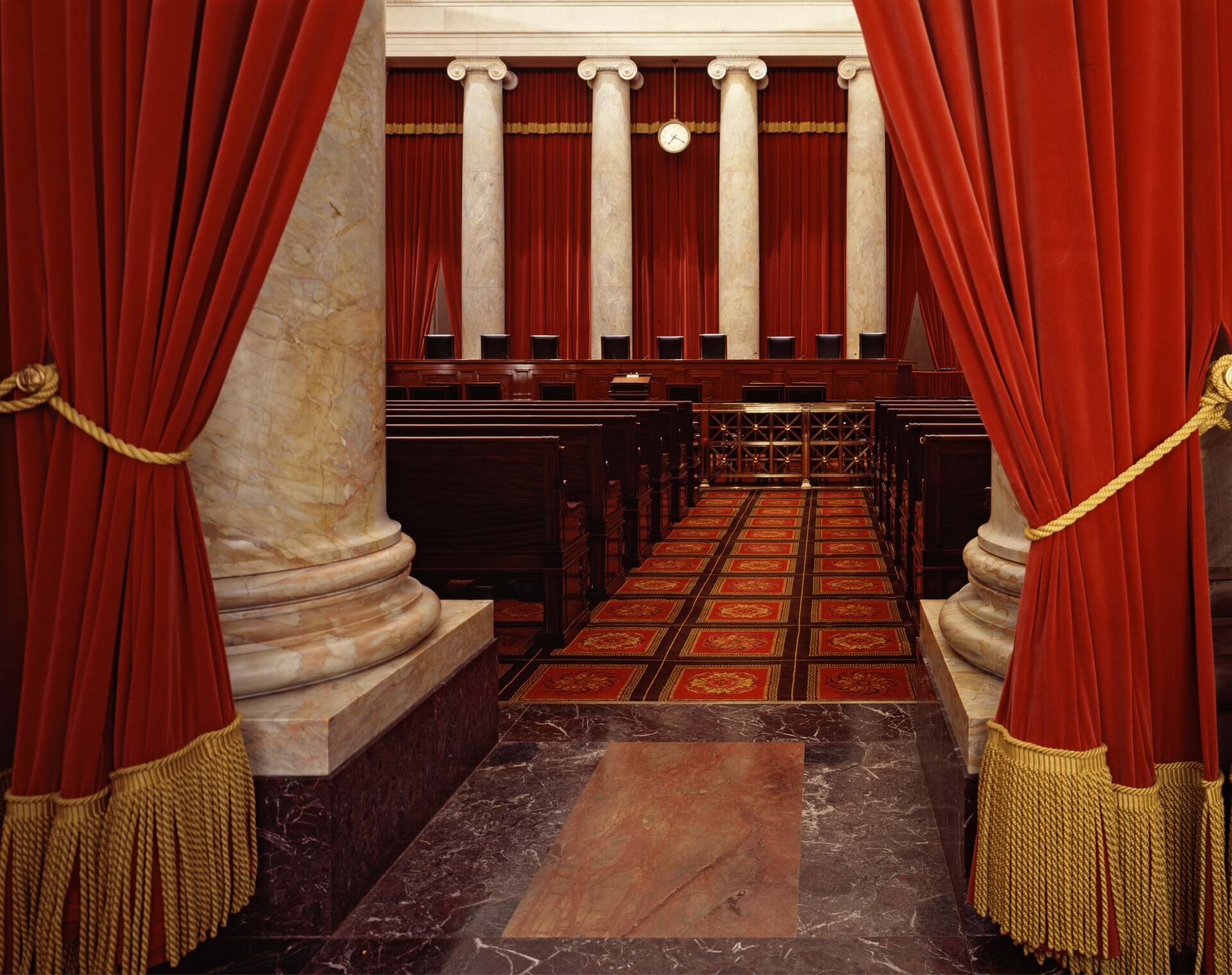The courtroom bench of the Supreme Court of the United States, framed by the red velvet curtains at the entrance to the chamber.